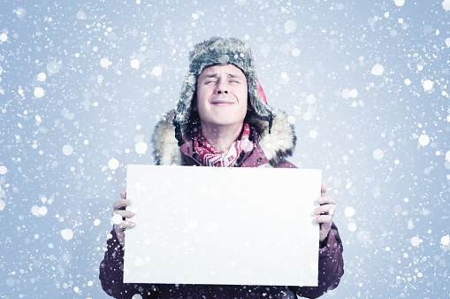 Frozen man with his eyes closed in winter clothes holds a white banner in his hands, there is snow on a blue background around