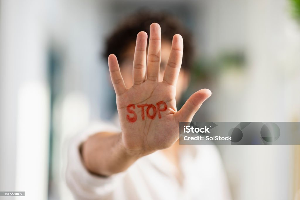 Stop! A medium, portrait shot of an unrecognisable mixed-race man holding his hand out to the camera, written on it is "STOP" in red marker. Bullying Stock Photo
