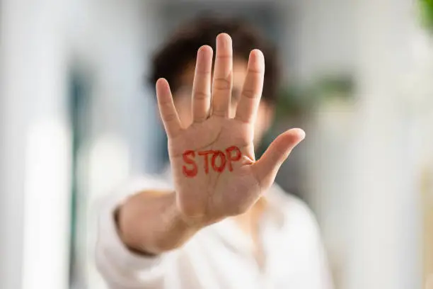 A medium, portrait shot of an unrecognisable mixed-race man holding his hand out to the camera, written on it is "STOP" in red marker.