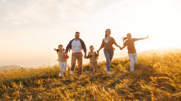 Happy family running in field in summer evening Happy young parents with children in casual clothes running with holding hands while enjoying time together on meadow in summer evening big family sunset stock pictures, royalty-free photos & images