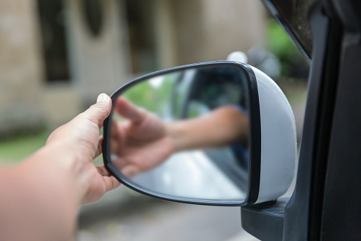 Close-up shot of unrecognizable driver hand adjusting side mirror outside the car