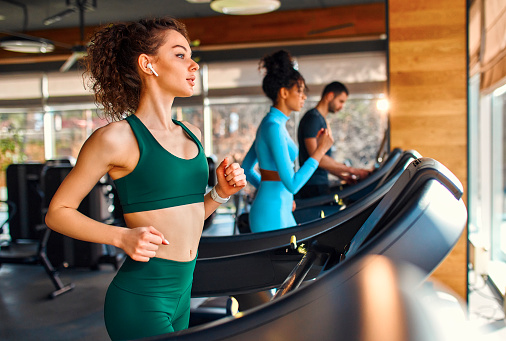 A group of multiethnic young people running on a treadmill in the gym. Cardio workout. The concept of sports and recreation.