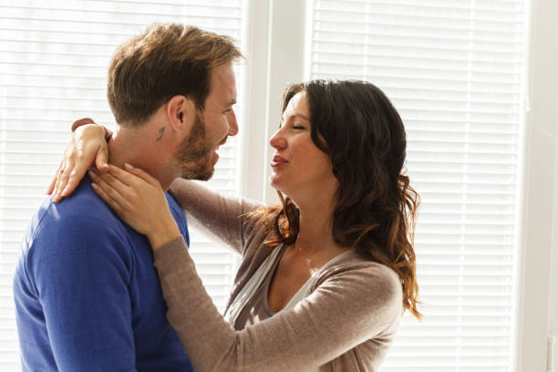istock Couple standing by the window, smiling at each other and embracing 1417276806