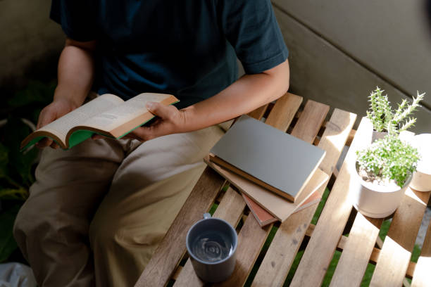 hombre asiático leyendo un libro en una mesa en el patio trasero. - outdoors book reading accessibility fotografías e imágenes de stock