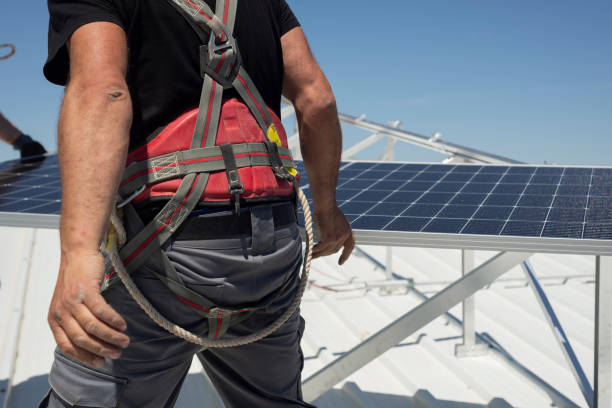 A worker in a harness holds solar panels on a rooftop. Renewable energy concept stock photo
