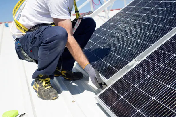 A worker installs solar panels on a rooftop. Renewable energy concept