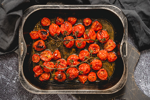 Baking tray with roasted cherry tomatoes with garlic, olive and thyme. Top view, flat lay