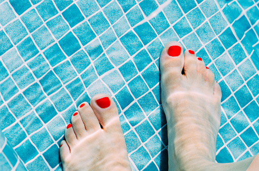 Close up of woman's feet with red nail polish in a pool with blue tiles - holiday or vacation concept