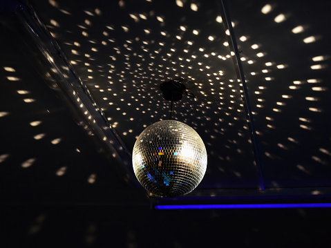 Shiny disco ball on the ceiling with reflections and shadows on black background