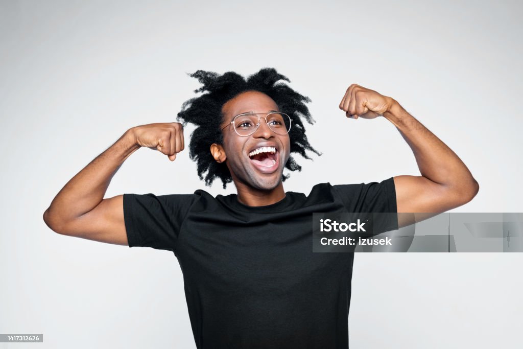 Headshot of excited man in black outfit Handsome afro american young man wearing black t-shirt, flexing his muscles and laughing. Studio shot on white background. 30-34 Years Stock Photo