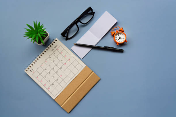 istock November 2022 desk calendar with alarm clock set at 9 o'clock and notepad on blue background. Directly above. Flat lay. Copy space. 1417312802