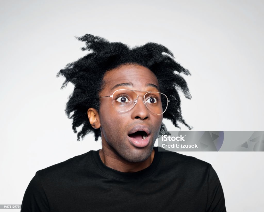 Headshot of surprised man in black outfit Handsome afro american young man wearing black t-shirt, looking away with mouth open. Studio shot on white background. Eyeglasses Stock Photo
