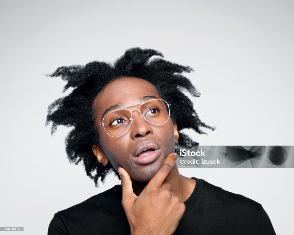 Headshot of worried man in black outfit Handsome afro american young man wearing black clothes, standing with hand on chin and looking away. Studio shot on white background. Inventor Stock Photo