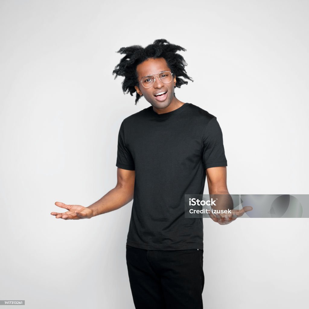 Portrait of displeased man in black outfit Upset afro american young man wearing black clothes, looking at camera. Studio shot on white background. Displeased Stock Photo
