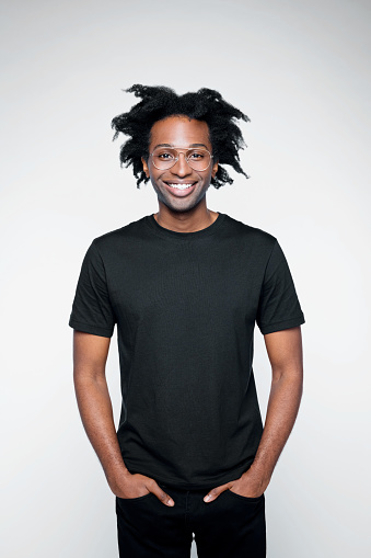 Cheerful afro american young man wearing black clothes, standing with hands in pockets and laughing at camera. Studio shot on white background.