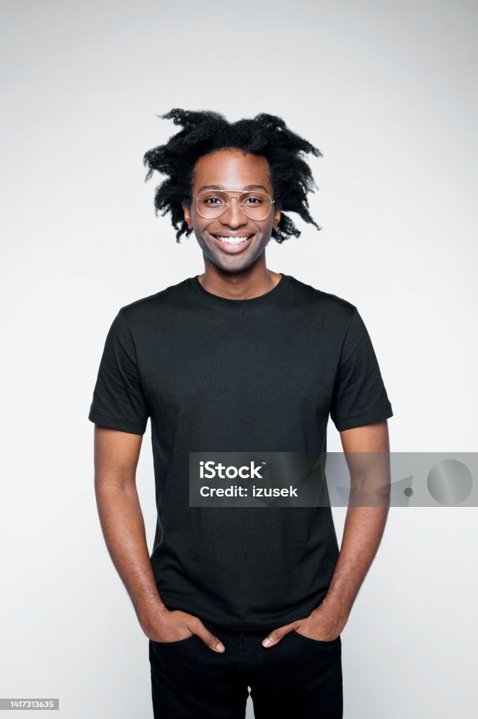 Portrait of handsome man in black outfit Cheerful afro american young man wearing black clothes, standing with hands in pockets and laughing at camera. Studio shot on white background. Black Color Stock Photo