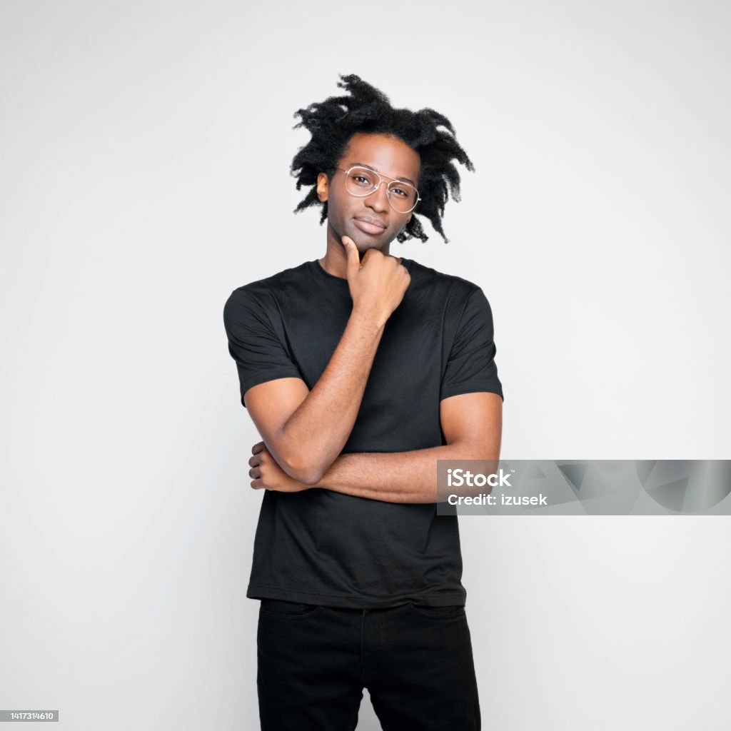 Portrait of thoughtful man in black outfit Handsome afro american young man wearing black clothes, standing with hand on chin and looking at camera. Studio shot on white background. 30-34 Years Stock Photo