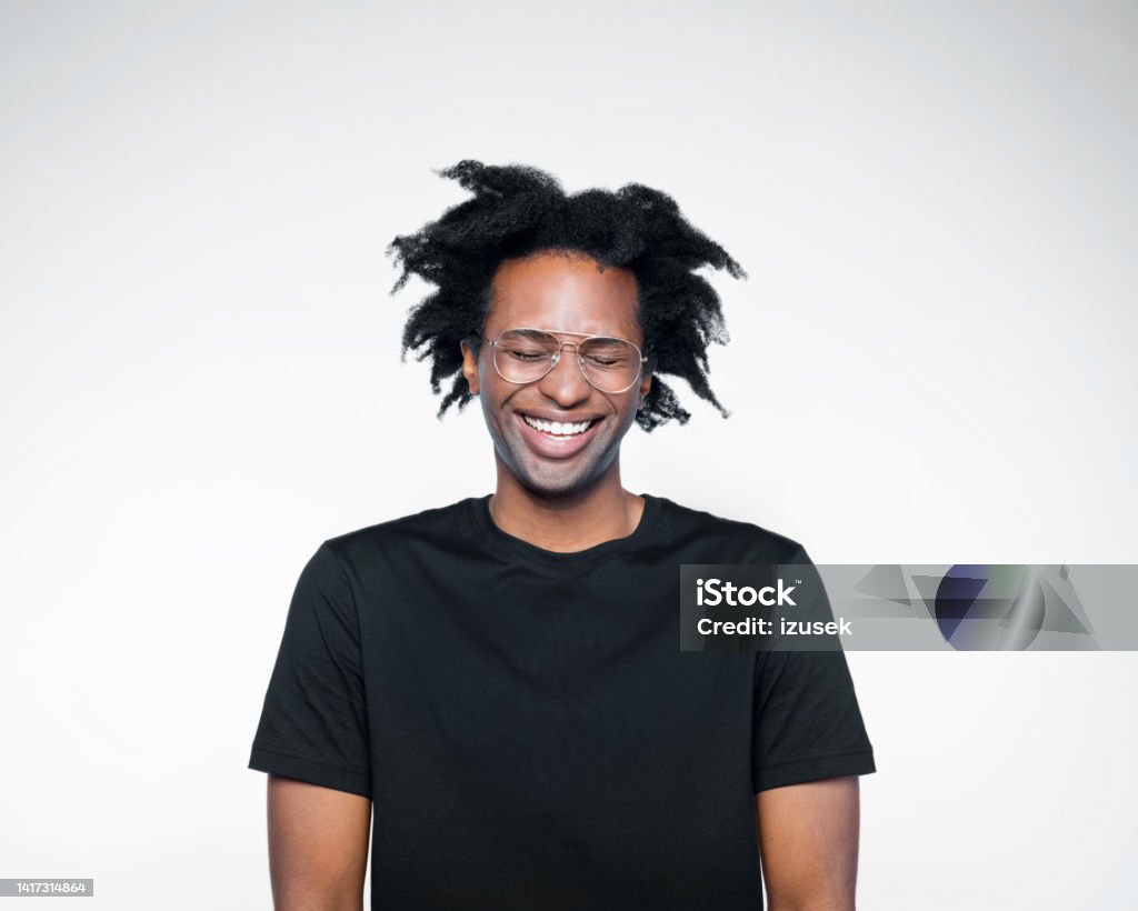 Potrait of happy man in black outfit Excited afro american young man wearing black t-shirt, laughing with eyes closed. Studio shot on white background. Ecstatic Stock Photo