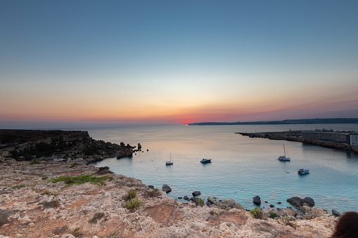 A colourful sunset over the cliffs of Paradis bay in Malta with a view on the Island of Gozo in the Mediterranean Sea. In summer the countries around the Mediterranean enjoy every evening these sunset