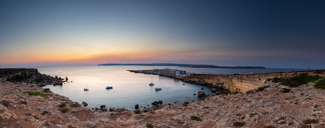 A colourful sunset over the cliffs of Paradis bay in Malta with a view on the Island of Gozo in the Mediterranean Sea. In summer the countries around the Mediterranean enjoy every evening these sunset