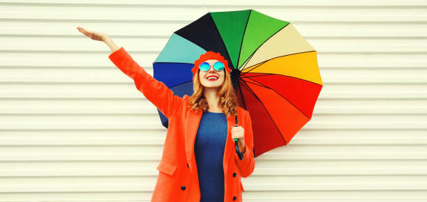 Autumn portrait of happy cheerful smiling young woman with colorful umbrella wearing red coat and beret on white background stock photo