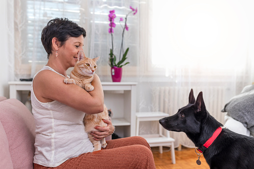 Mature woman petting her cat and dog at home