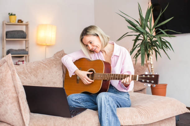 istock Middle aged woman practicing and learning how to play guitar on laptop 1417335212