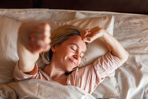 Mujer feliz de mediana edad se sienta en la cama y estira los brazos photo