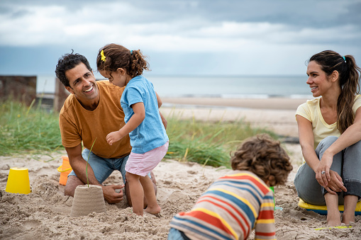 A shot of a Hispanic family sitting down on the sand at a beach in Seahouses, Northumberland. They are playing together and building sand castles with beach buckets.