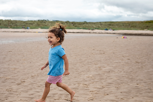 A shot of a young Hispanic girl playing at a beach in Seahouses, Northumberland.  She is walking on the sand with a big smile on her face.