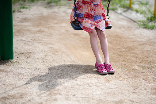 Feet and shadow of a child playing on a swing