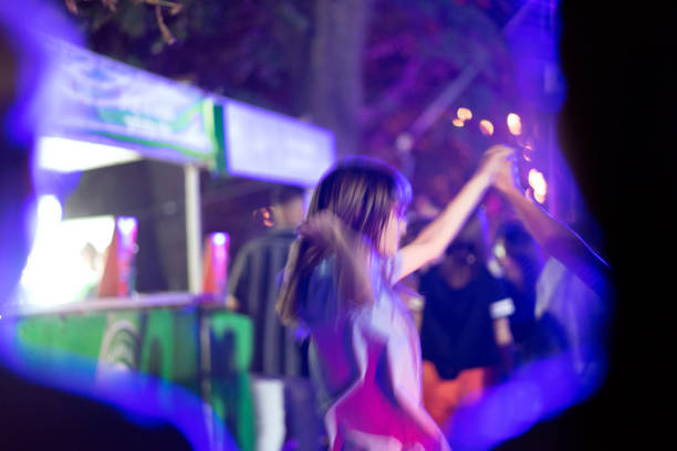 Two Asian and Caucasian girls dance in the crowd and enjoy the atmosphere at a music festival. Blurred motions.