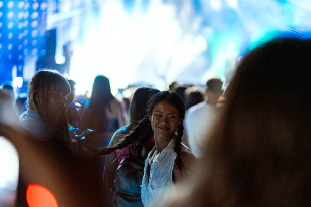 Two Asian and Caucasian girls dance in the crowd and enjoy the atmosphere at a music festival.