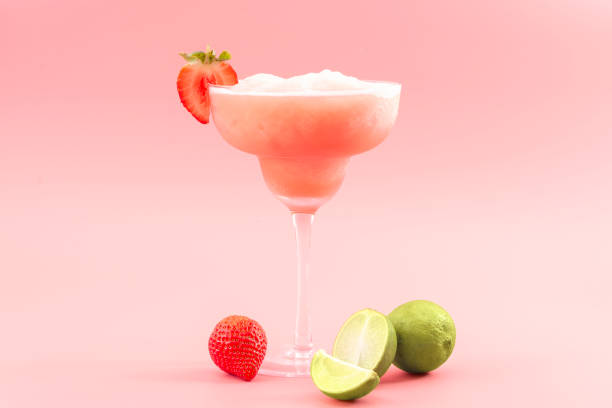 mixed cocktails, party punch smoothies and frozen summer drinks concept with strawberry mojito or daiquiri in margarita glasses, strawberries and limes isolated on pink background - mocktail fotos stockfoto's en -beelden