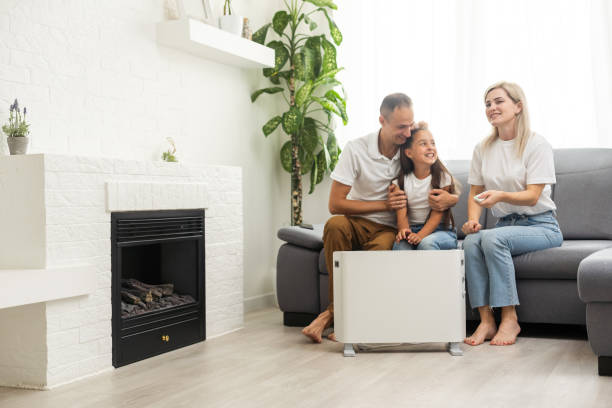 Electric heater at home. Young family warms near a heating radiator. Electric heater at home. Young family warms near a heating radiator space heater stock pictures, royalty-free photos & images