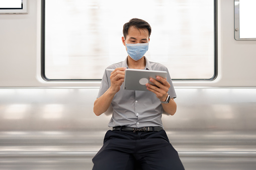 Man wearing mask using tablet while taking subway