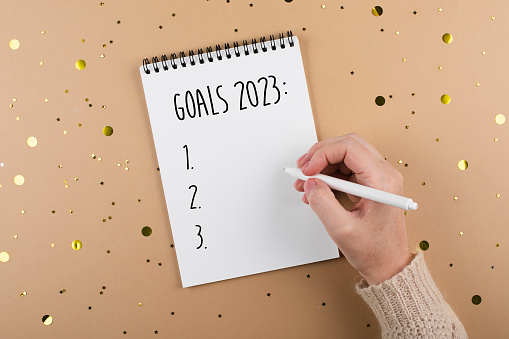 New Year goals 2023. Woman's hand writing in note pad goals list. Concept of new year planning. Flat lay, top view