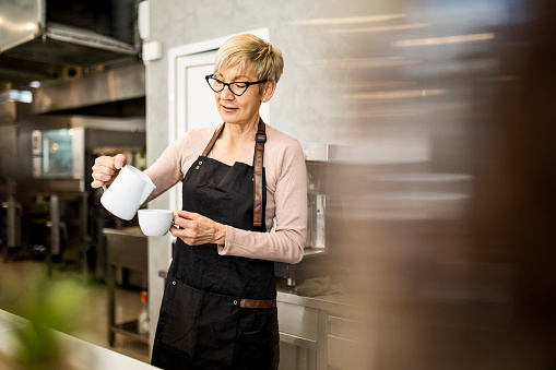 Mature barista preparing coffee for customers at her cafe counter
