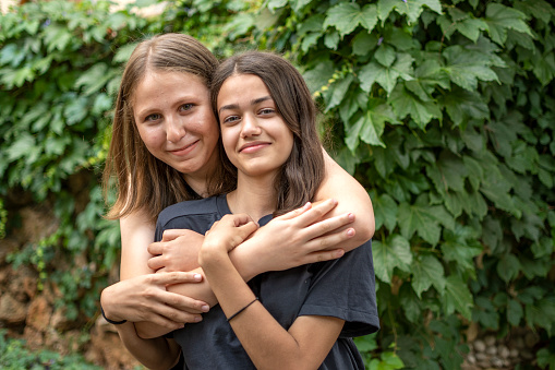 Two Young Girls Giving One Another Hug In Summer Field Smiling To Camera