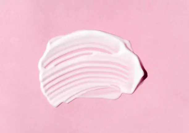 Texture of white cream on pink background. Smear of moisturizer closeup. Lotion swatch. Beauty, skin care product smear smudge drop. SPF sunscreen cream sample