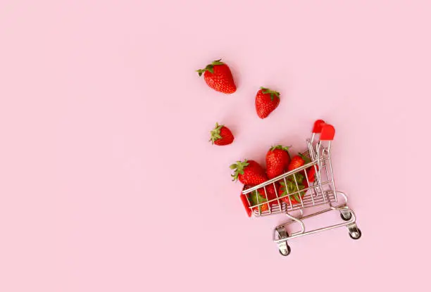 Fresh red strawberry in shopping cart on pink background. Online shopping and Valentines Day minimalistic concept. Black Fridays sales banner. Healthy, organic, vegan food