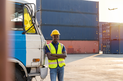 An African truck driver stood resting and smiling happily beside the truck. at the container warehouse