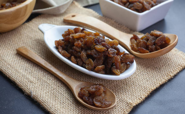 Raisins stacked in a white bowl next to some wooden spoons Raisins stacked in a white bowl raisin stock pictures, royalty-free photos & images
