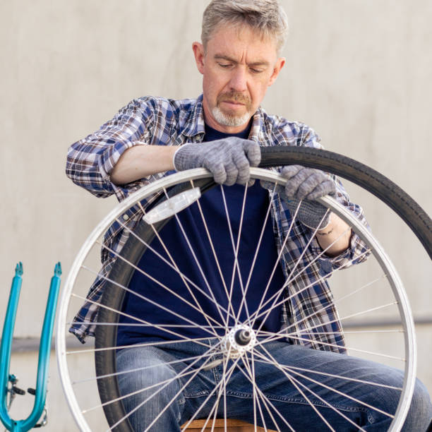 50 year old bearded man in a plaid shirt repairing a bicycle wheel