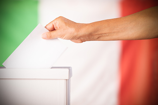 Hand person putting ballot in a box during elections in italy in front of flag