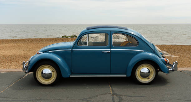 classic  blue  vw beetle parked on seafront promenade with sea and beach in background. - beetle imagens e fotografias de stock