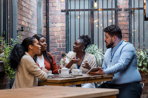 Medium shot of a group of co-workers having coffee/tea together on an outdoor terrace in the North East of England. They are having a business meeting, talking together while looking at a digital tablet.