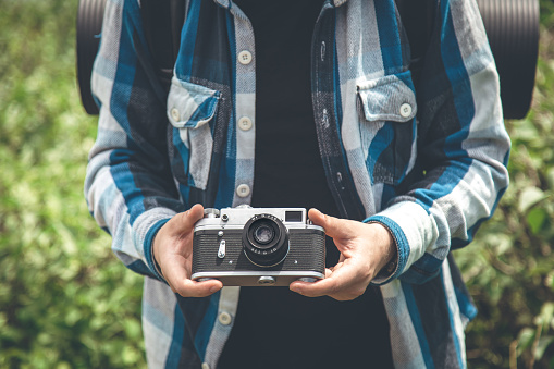 Vintage film camera in the hands of a man on a blurred background, the concept of tourism and camping.