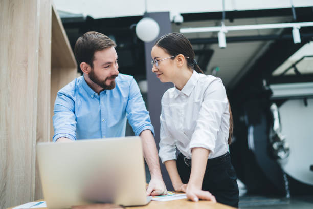istock Pleased adult employees looking at each other while having discussion and using laptop in office 1417378890