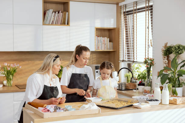 istock Beautiful young mother holding whisk in hand whisking eggs for preparing dough baking. Curious small daughter listening to watching process. Serious wise gerandmother helping 1417381050
